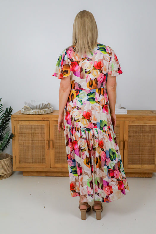 Woman wearing a colorful floral dress standing in front of wooden cabinets.
