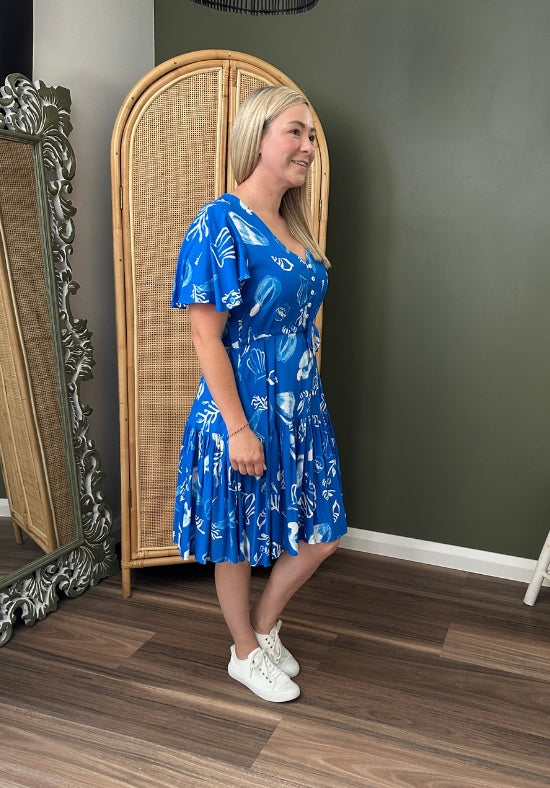 Woman in a blue dress standing in front of a mirror in a room with a dark green wall.