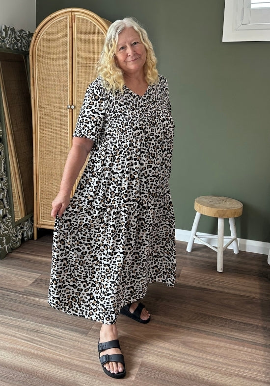 Woman wearing a black and white patterned dress standing in a room with a wooden floor and green wall.