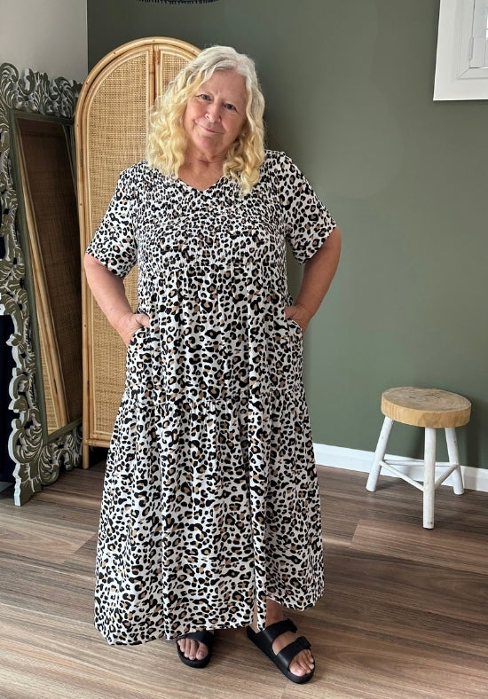 Woman wearing a leopard print dress standing in a room with a green wall and wooden floor.