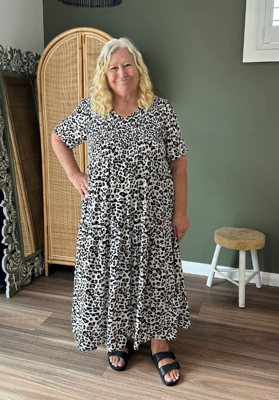 Woman wearing a black and white patterned dress standing in a room with a green wall and wooden floor.