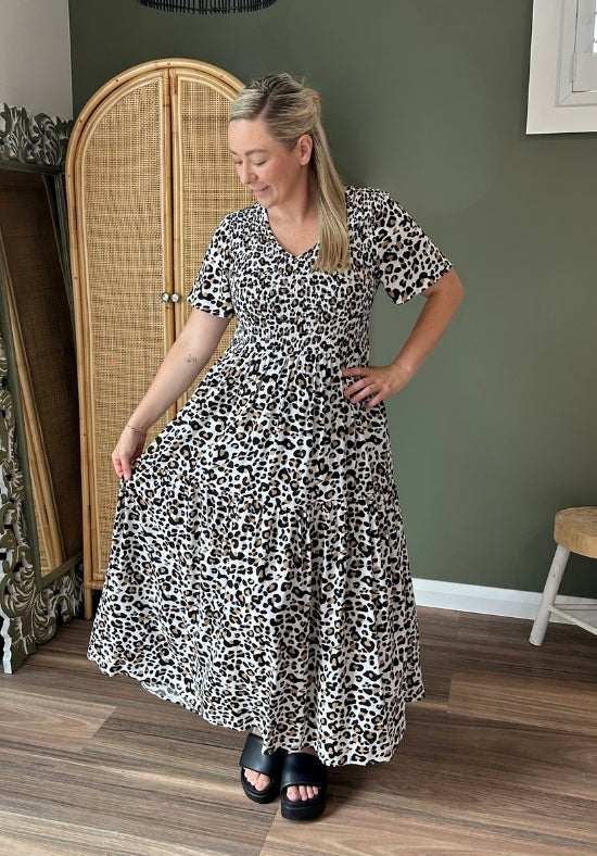 Woman wearing a black and white patterned dress in a room with a wicker wardrobe and wooden floor.