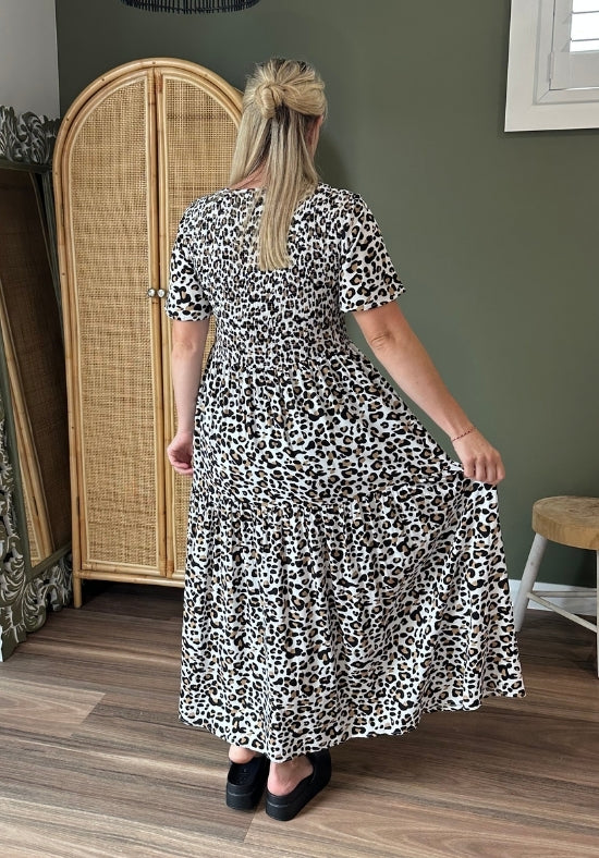 Woman wearing a black and white patterned dress in a room with a wooden floor and a rattan cabinet.