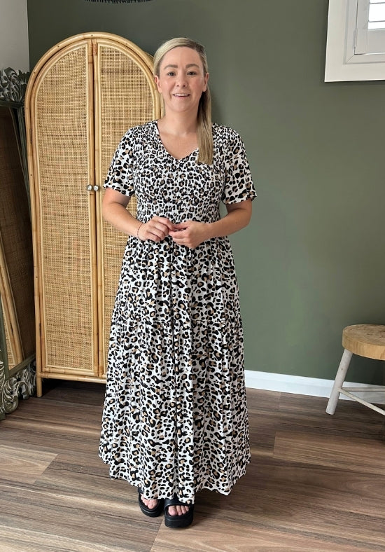 Woman wearing a black and white patterned dress standing in a room with a green wall and wooden floor.