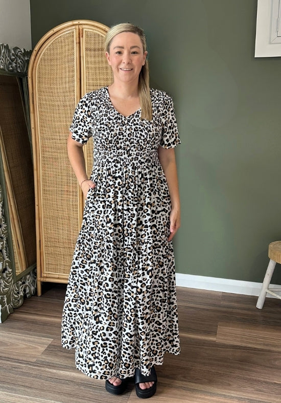 Woman wearing a black and white patterned dress standing in a room with a green wall and wooden floor.