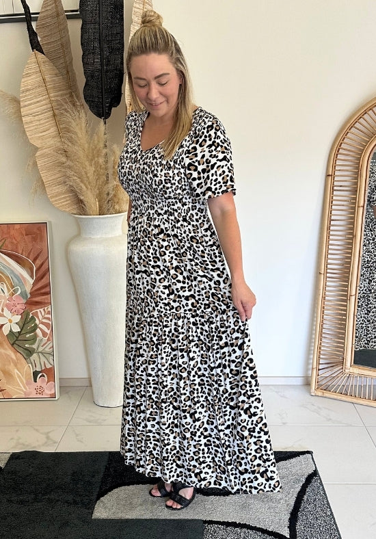 Woman wearing a leopard print dress standing in a room with decor elements.