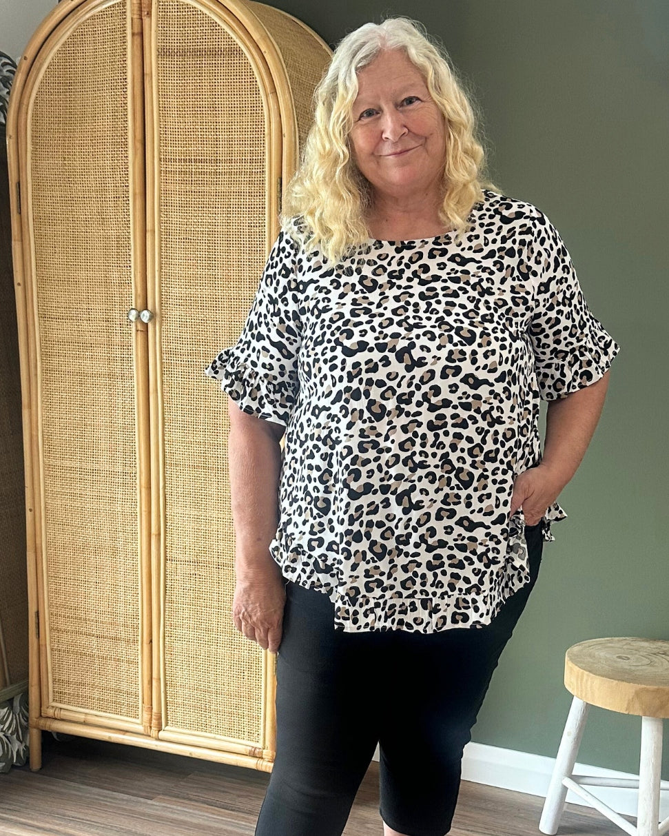 Woman wearing a leopard print top and black leggings standing in front of a rattan wardrobe.