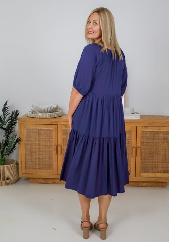 Woman wearing a blue dress standing in front of wooden cabinets.