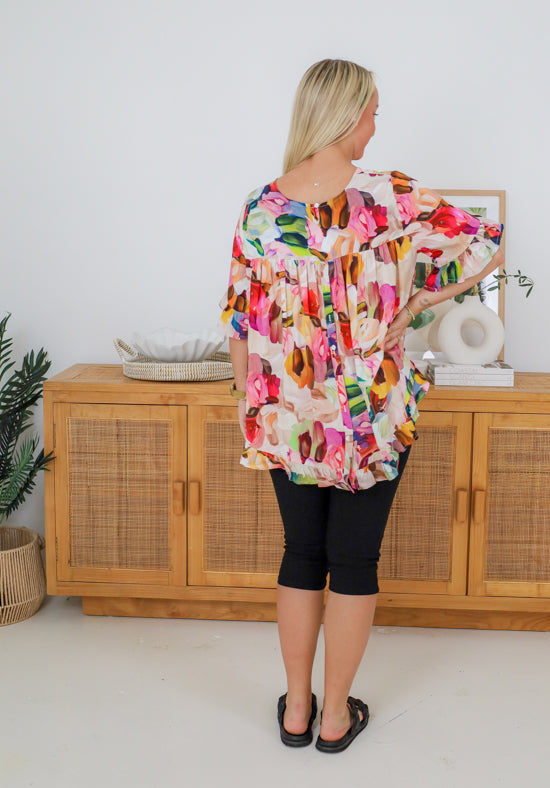 Woman wearing a colorful floral blouse in a room with wooden furniture.