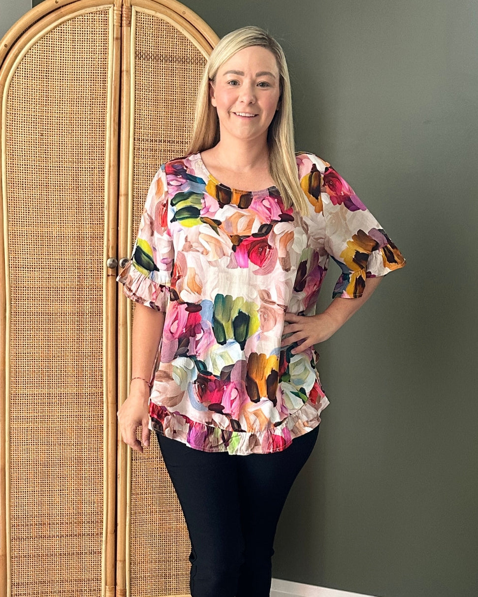 Woman wearing a colorful floral blouse standing against a dark wall.