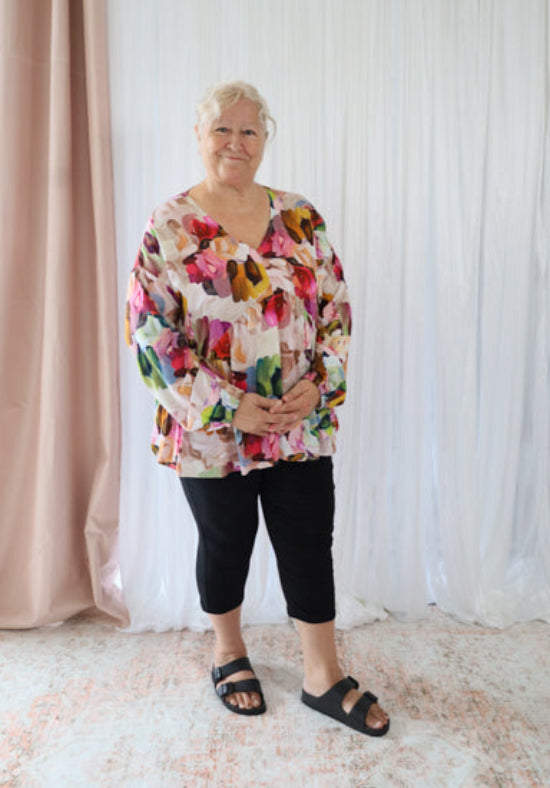 Woman wearing a colorful floral blouse against a white curtain background