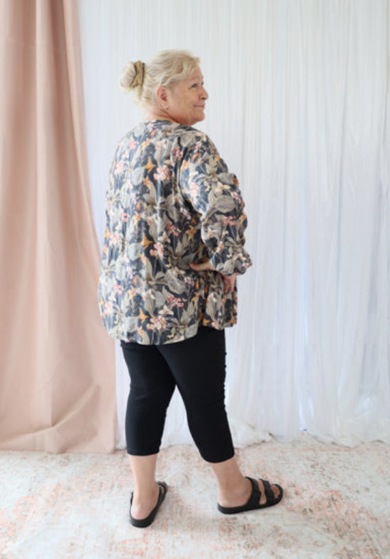 Person wearing a floral jacket standing against a white curtain.