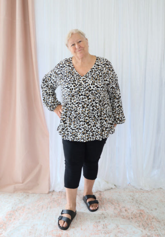 Person wearing a leopard print top and black leggings standing against a light curtain background