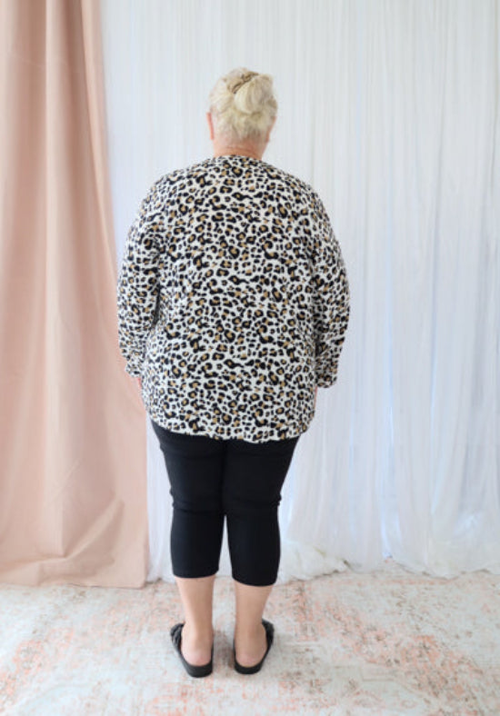 Person wearing a leopard print shirt and black pants standing against a white curtain.