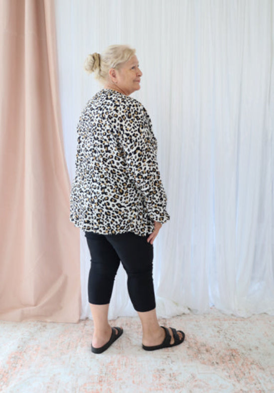 Person wearing a leopard print jacket and black pants standing against a white curtain.