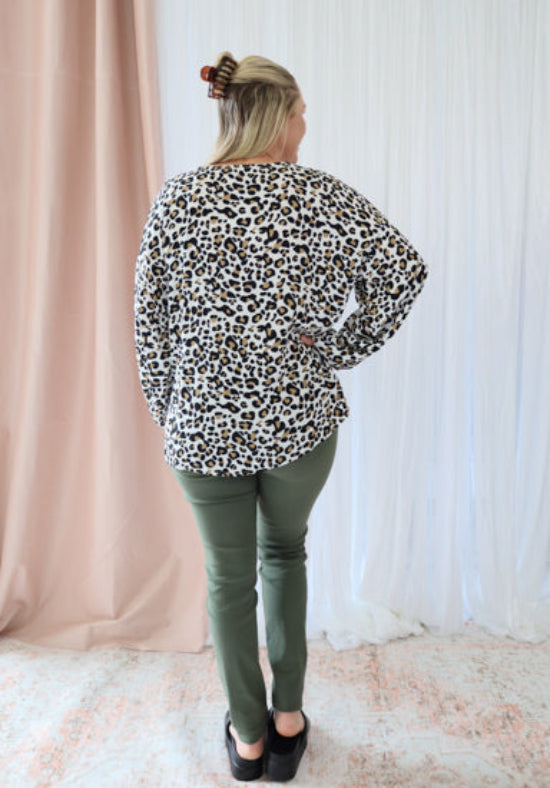 Person wearing a leopard print shirt and green pants standing against a white curtain.