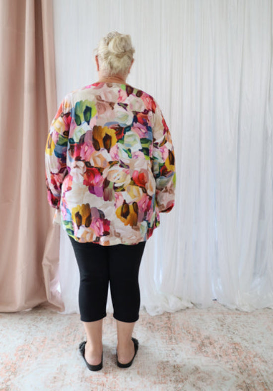 Person wearing a colorful floral jacket standing in front of a white curtain.
