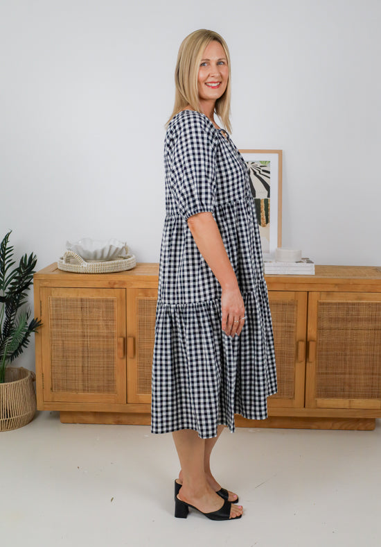 Woman wearing a black and white checkered dress standing in a room with wooden furniture and decor.