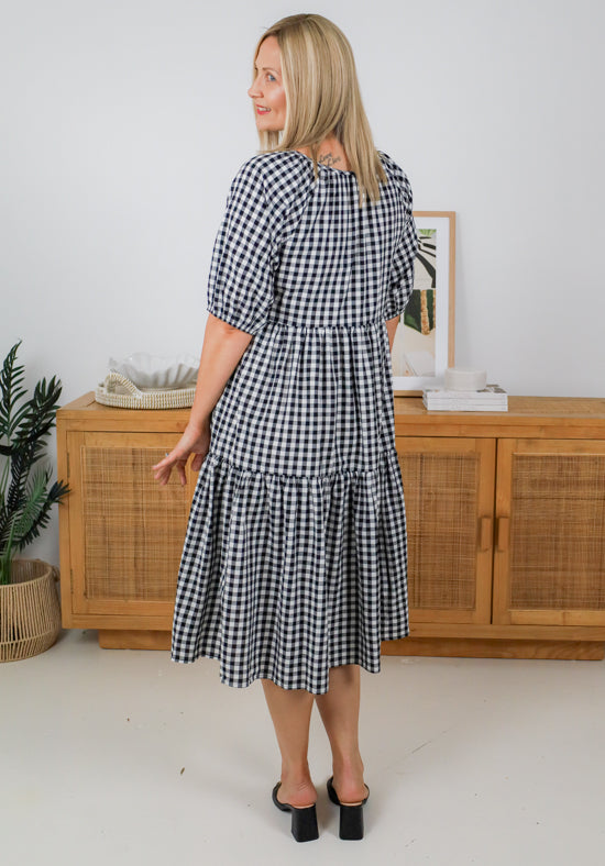 Woman wearing a black and white checkered dress in a room with wooden furniture and decor.