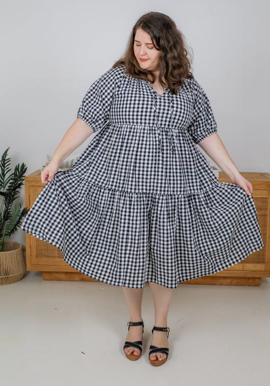 Woman wearing a black and white checkered dress standing in a minimal indoor setting.