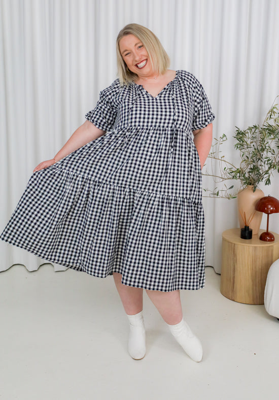 Woman wearing a black and white checkered dress in a minimalistic room.
