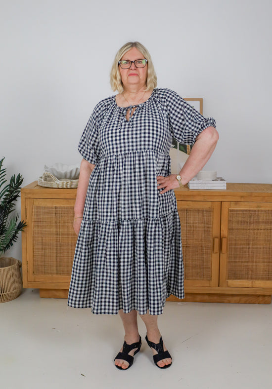 Woman wearing a black and white checkered dress standing in a room with wooden furniture.