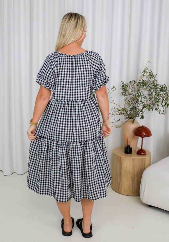 Woman wearing a black and white checkered dress in a room with a curtain and plant.