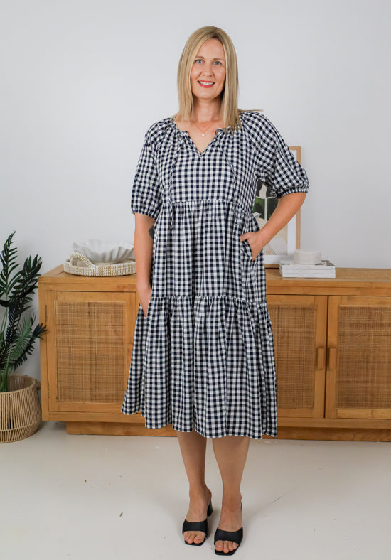 Woman wearing a black and white checkered dress standing in a room with wooden furniture and decor.