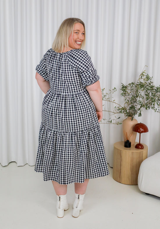 Woman wearing a black and white checkered dress in a minimalistic room.