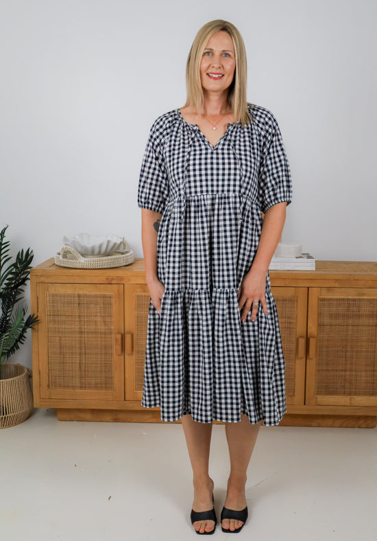 Woman wearing a black and white checkered dress standing in front of a wooden cabinet.