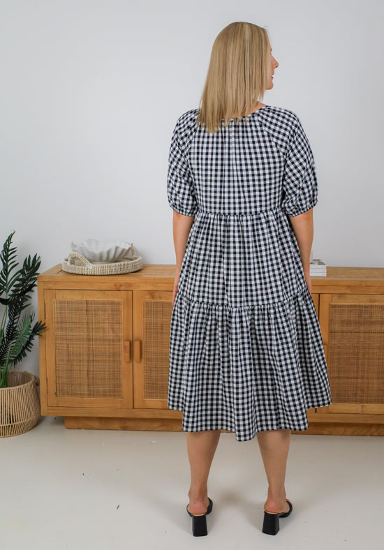 Woman wearing a black and white checkered dress standing in front of a wooden cabinet.