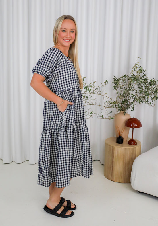 Woman wearing a black and white checkered dress in a room with plants and a side table.